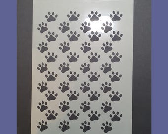 Könnte beinhalten: Eine weiße Schablone mit einem sich wiederholenden Muster aus schwarzen Pfotenabdrücken. Die Schablone ist für Bastel- und Dekorationsarbeiten konzipiert.