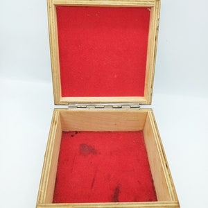 Puede incluir: Una caja de madera con tapa con bisagras y un interior de terciopelo rojo. La caja tiene un dise&ntilde;o decorativo en la parte delantera.