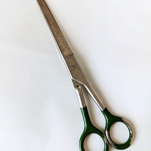 Könnte beinhalten: Eine silberne Schere mit grün lackierten Griffen. Die Schere hat eine lange Klinge und ist geöffnet.