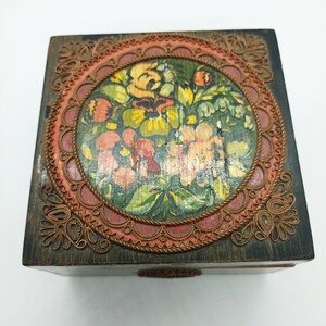 Puede incluir: Una caja de madera con un dise&ntilde;o floral pintado dentro de un marco circular. El marco est&aacute; decorado con un ribete tejido de cobre y rojo.