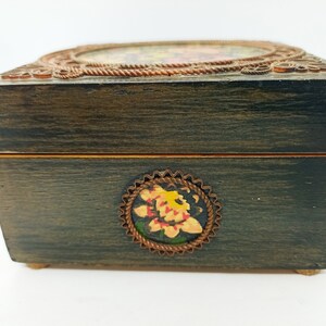 Puede incluir: Una caja de madera con un acabado marr&oacute;n oscuro y un dise&ntilde;o floral en la parte delantera. La caja tiene una tapa con bisagras y un ribete met&aacute;lico decorativo alrededor de los bordes.