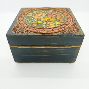 Puede incluir: Una caja de madera verde oscuro con una tapa con bisagras. La tapa presenta un dise&ntilde;o circular con un patr&oacute;n floral en tonos rojos, naranjas, amarillos y verdes. La caja tiene un borde dorado.