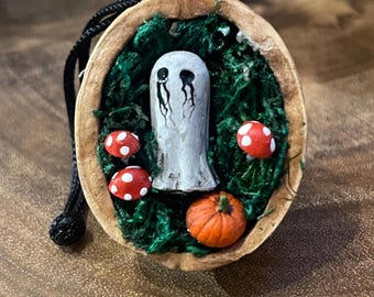 Walnut shell with extra spooky black-eyed ghost on a bed of moss with pumpkin and toadstool. Quirky Halloween decoration.