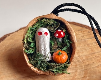 Walnut shell with red-eyed ghost on a bed of moss with pumpkin and toadstool. Quirky Halloween decoration.