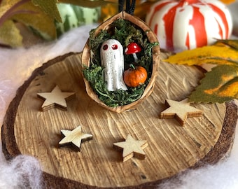 Walnut shell with red-eyed ghost on a bed of moss with pumpkin and toadstool. Quirky Halloween decoration.