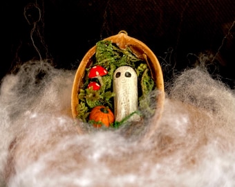 Walnut shell with black-eyed ghost on a bed of moss with pumpkin and toadstool. Quirky Halloween decoration.