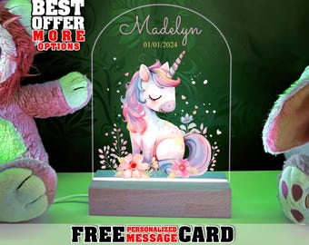 May include: Personalized night light with a unicorn design. The light features a white unicorn with a pink mane and tail, surrounded by flowers and greenery. The text "Madelyn 01/01/2024" is printed on the light.