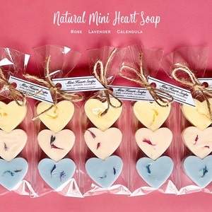 May include: Mini heart-shaped soaps in clear cellophane bags tied with twine. The soaps are in three colors: yellow, pink, and blue, each with floral accents. The text "Natural Mini Heart Soap" is at the top.