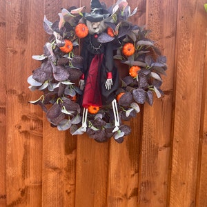 Halloween wreath with artificial black eucalyptus with pumpkins and skeleton witch for front door