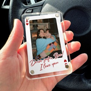 May include: Clear acrylic playing card with a photo of a couple hugging and kissing. The card has the Ace of Hearts and Six of Clubs symbols. Text in red cursive reads "Drive safe, Bae! I love you."