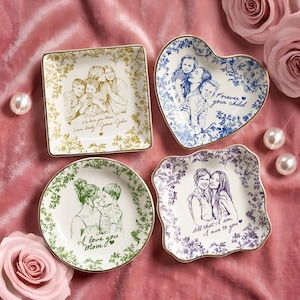 May include: Four decorative ceramic plates with gold rims, each featuring a family portrait sketch. The plates are square, heart-shaped, and round, with floral patterns and text: "We love you Mom," "Forever your child," "I love you Mom," and "All that I am, I owe to you."