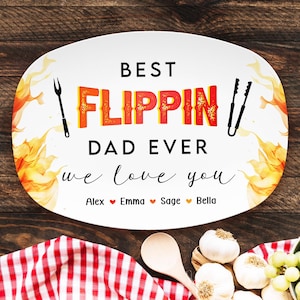 May include: White oval platter with the text "BEST FLIPPIN DAD EVER we love you" in black and orange. Includes names Alex, Emma, Sage, and Bella. Features a fork and tongs illustration. Decorative flames surround the edges.