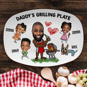 May include: Oval white ceramic plate with the text "DADDY'S GRILLING PLATE". The plate features a cartoon illustration of a man grilling with his family and dog. The names "Ennie", "John", "Annie", and "Rex" are also on the plate.
