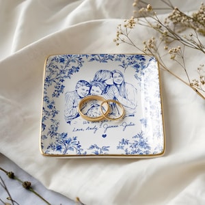 May include: Square ceramic trinket dish with a blue floral border and a gold rim. The center features a family portrait and the text "We love you... Love, Andy, James, Julia". Two gold rings rest on the dish.