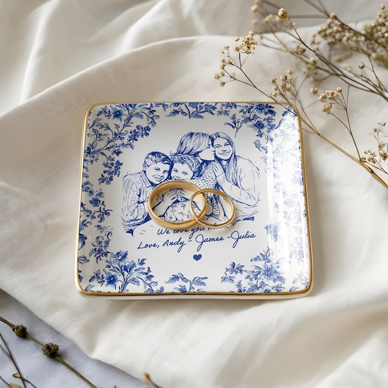 May include: Square ceramic trinket dish with a blue floral border and a gold rim. The center features a family portrait and the text "We love you... Love, Andy, James, Julia". Two gold rings rest on the dish.