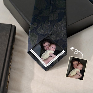 May include: Navy blue patterned tie with a photo of a man holding a baby. The tie has the text "DAD, THE FIRST MAN I HAVE EVER LOVED" and "FOREVER YOUR LITTLE GIRL, 11.12.2025". A small photo is next to the tie.