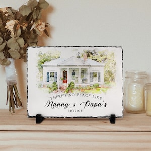 May include: A watercolour painting of a white house with a porch and green trees. The house is on a slate plaque with the text "There's no place like Nanny & Papa's House".