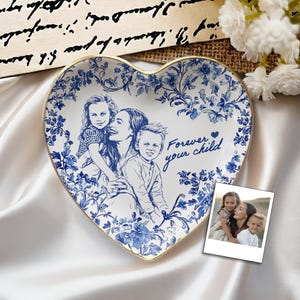 May include: Heart-shaped ceramic plate with a blue and white floral design and a gold rim. The plate features a family portrait and the text "Forever your child". A small photo is next to the plate.