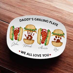May include: White ceramic plate with the text "DADDY'S GRILLING PLATE" and the phrase "WE ALL LOVE YOU". The plate features illustrations of burgers and hot dogs with names: John, Mark, Annie, and Rex.