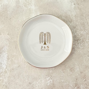May include: White ceramic dish with a gold rim and a gold weeping willow tree design. The dish has the initials "J & S" and the text "SINCE 2016" in gold. The dish has an irregular, organic shape.