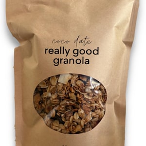 K&ouml;nnte beinhalten: Ein brauner Standbeutel aus Papier mit Granola, der ein ovales Sichtfenster besitzt, durch das der Inhalt zu sehen ist. Der Aufdruck auf der Vorderseite lautet "coco date really good granola" und "12 oz" in schwarzer Schrift.