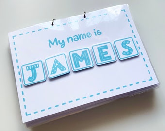May include: A white rectangular card bound with metal rings, featuring the light blue text "My name is" above five square tiles spelling "JAMES". Each letter tile has a unique light blue pattern, including stripes, stars, and swirls.