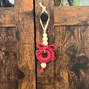 Peut inclure: Une couronne en macramé rouge et blanche avec des perles en bois suspendues à un bouton de porte.