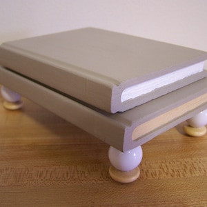 May include: A rectangular riser platform constructed from two stacked, light gray painted wooden blocks. The structure is supported by four white spherical feet, each resting on a small, flat, light-colored wooden circular base.