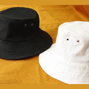 May include: Two bucket hats, one black and one white, with silver eyelets. The hats are made of a soft, cotton fabric.