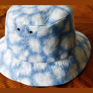 May include: A blue and white tie-dye bucket hat with a wide brim. The hat has two silver eyelets on the crown.
