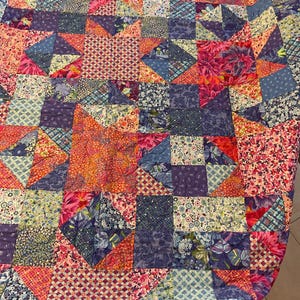 May include: A patchwork quilt with a vibrant mix of floral and geometric patterns in shades of pink, blue, purple, and orange. The quilt features a variety of fabric textures and designs, creating a visually rich and textured textile.