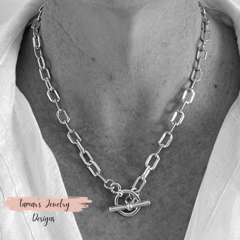 May include: A silver chain necklace with a toggle clasp. The chain is made of rectangular links.