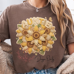 May include: Brown t-shirt with a sunflower design and the word "AUNTIE" in yellow letters. The sunflower is made of yellow and tan fabric patches. The text "Design Only" is written in cursive below the sunflower.