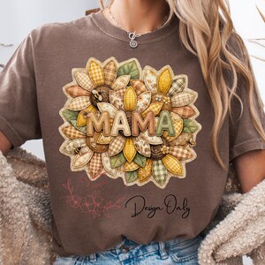 Puede incluir: Camiseta marrón con un diseño de girasol y la palabra "MAMA". El girasol tiene un diseño de patchwork con colores amarillo, verde y marrón. La camiseta también tiene el texto "Design Only" en una fuente cursiva.
