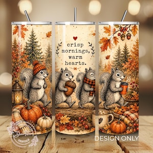 Pode incluir: Um copo cil&iacute;ndrico com palhinha apresentando uma ilustra&ccedil;&atilde;o de outono com esquilos, ab&oacute;boras, pinheiros e folhas ca&iacute;das. O texto diz crisp mornings, warm hearts. O design inclui uma lanterna, bolotas e uma caneca de caf&eacute;.