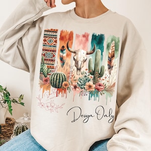 May include: Beige sweatshirt with a colorful design featuring a skull, cacti, feathers, and geometric patterns. The design is surrounded by flowers and has a watercolor effect. The text "Design Only" is printed below the design.