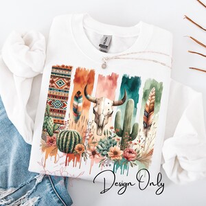 May include: A white t-shirt with a colorful design featuring a watercolor-style background with a skull, cactus, feathers, and geometric patterns. The text "Design Only" is printed at the bottom of the shirt.