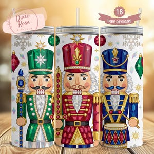 May include: Three stainless steel tumblers with festive nutcracker designs. Each tumbler features a different nutcracker soldier in vibrant colors: green, red, and blue. The tumblers are decorated with snowflakes and ornaments, perfect for holiday drinks.