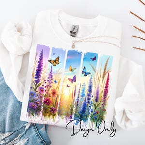 Puede incluir: Camiseta blanca con un dise&ntilde;o de acuarela de flores coloridas y mariposas. El dise&ntilde;o presenta una variedad de flores en tonos de morado, rosa y azul, con mariposas en tonos de amarillo, naranja y azul.