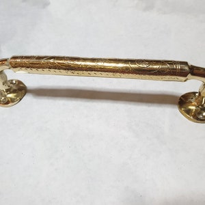 Könnte beinhalten: Ein goldfarbener Türgriff mit einem verzierten Design. Der Griff hat eine gebogene Form und zwei runde Enden.