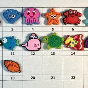 May include: A set of 24 colorful, small, plastic sea creature charms. The charms include a starfish, a crab, an octopus, a dolphin, a turtle, a seashell, a seahorse, a fish, a whale, and a jellyfish. The charms are numbered 1 through 24.