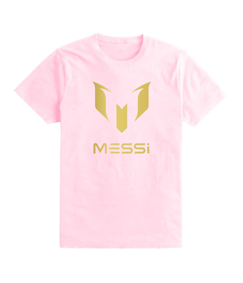 Op de afbeelding: Een roze T-shirt met een gouden logo van een gestileerde "M" en het woord "MESSI" eronder.