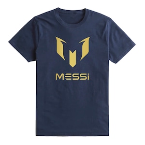 Op de afbeelding: Een marineblauw t-shirt met een gouden afbeelding van de letter "M" en het woord "MESSI" gedrukt op de voorkant.