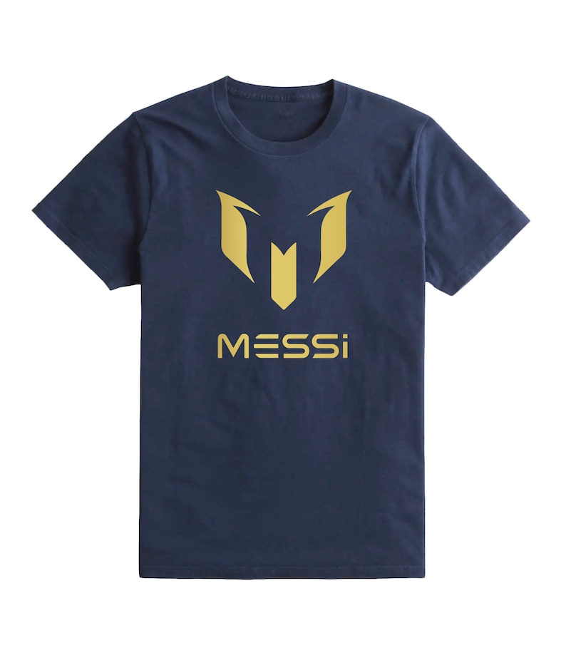 Op de afbeelding: Een marineblauw t-shirt met een gouden afbeelding van de letter "M" en het woord "MESSI" gedrukt op de voorkant.