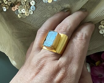 May include: A gold ring featuring a large, rectangular, light blue gemstone. The ring is worn on a finger.