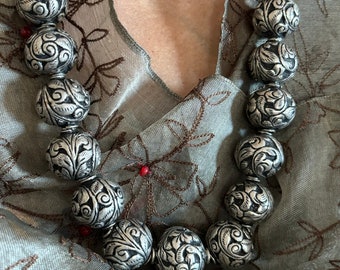 May include: A silver necklace with ornate, round beads. The beads have a floral design and are strung together on a silver chain.