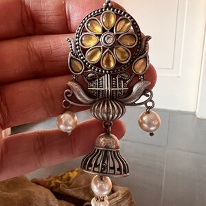 May include: Silver earrings with a floral design and yellow glass stones. The earrings have a bell-shaped dangle with three white pearls.