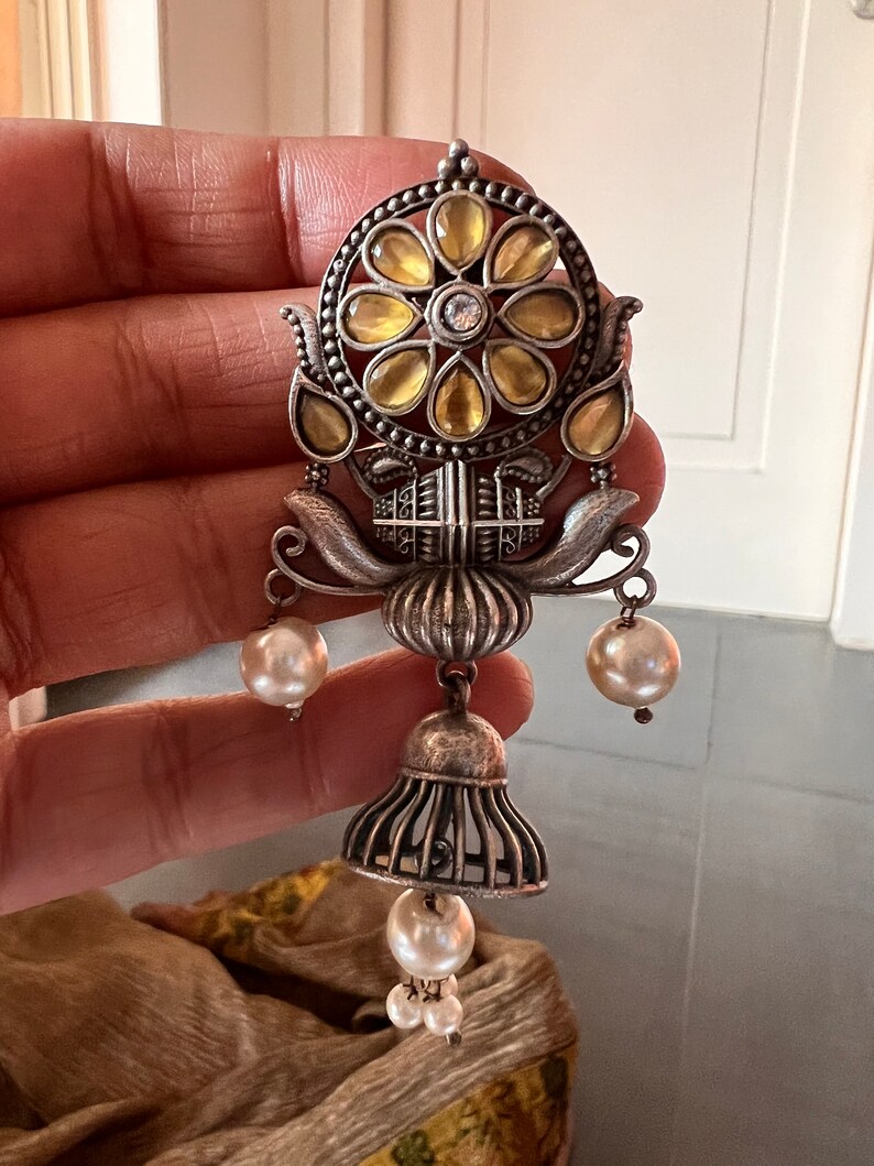 May include: Silver earrings with a floral design and yellow glass stones. The earrings have a bell-shaped dangle with three white pearls.