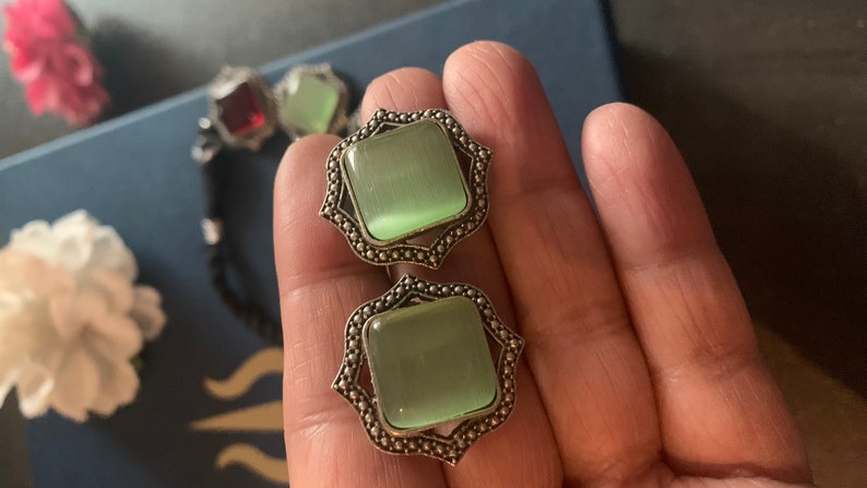 May include: A pair of silver earrings with green cat's eye stones set in a square shape with a decorative border.