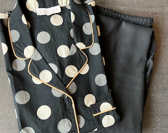 May include: Black and white polka dot pajama top with gold trim and matching black pajama pants. The top has a button closure and a collar. The brand name "SHIVKA" is visible on the top.